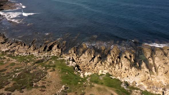 Stone peaks and seashore and foamy waves under cloudy sky