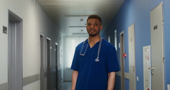 African American Doctor Looks Into the Camera Standing in a Corridor of Clinic