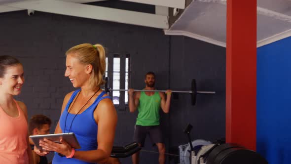 Female trainer interacting with woman while using digital tablet