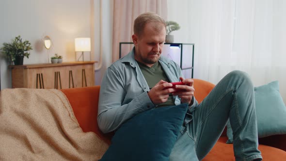 Worried Funny Adult Man Playing Shooter Online Video Games Celebrate Win on Mobile Phone at Home