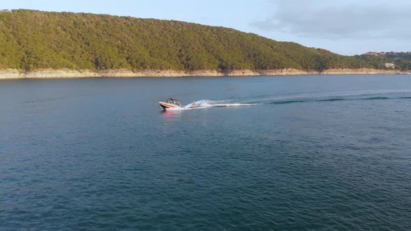 Side pan of a wakeboarder on Lake Travis. Cliffs and the oasis are seen in the background at golden