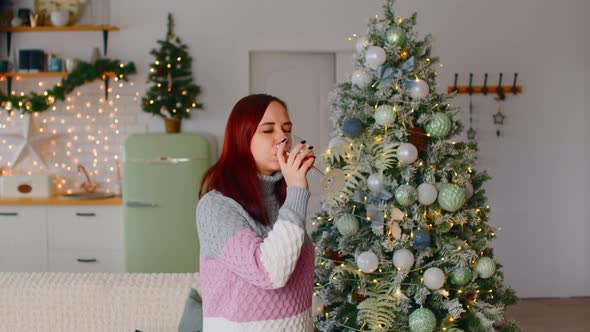 Young Woman Drinking Beverage and Dancing Near Christmas Tree in Living Room