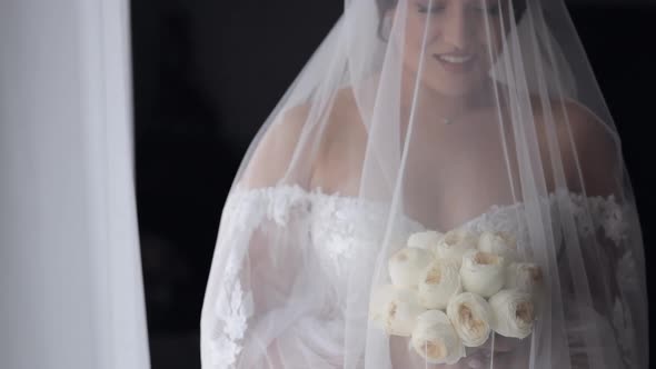 Bride in White Dress Staying Near Window with Flowers Bouquet Wedding Morning Preparations at Home