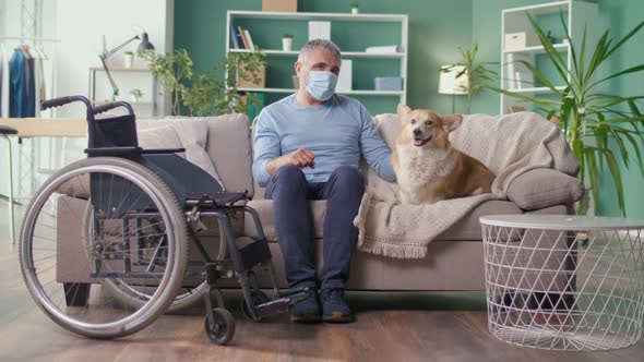 A Sad Elderly Man with Disabilities in a Medical Mask Stroking His Dog