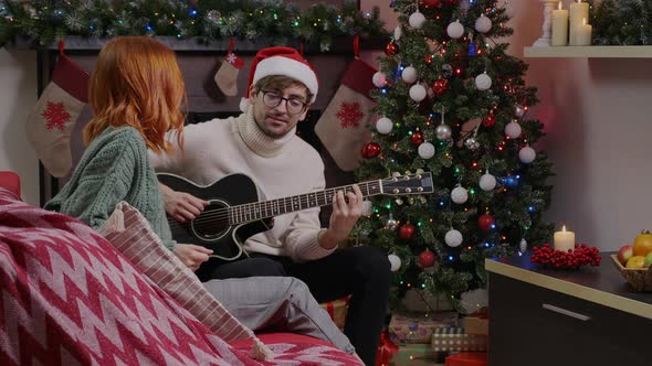 Side view of a couple playing the guitar keeping the rhythm of a Christmas song.