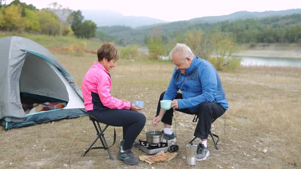 Happy Senior Couple Eating and Drinking While Camping Outdoor in Front of Lake Elderly Travel