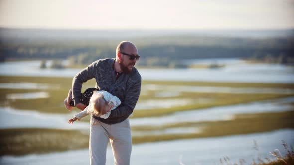 Young Father Playing with His Baby Daughter on the Field - Holding Her on His Hands