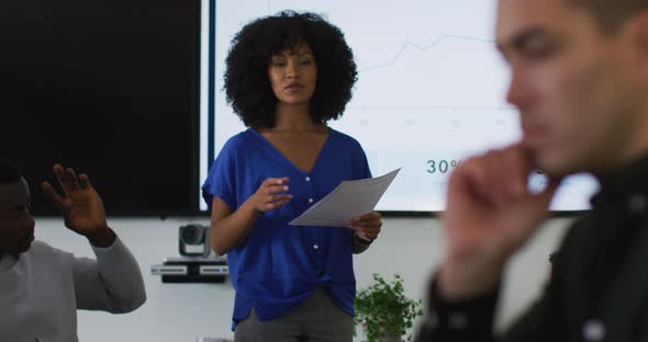 Mixed race businesswoman giving presentation to diverse group of colleagues in meeting room
