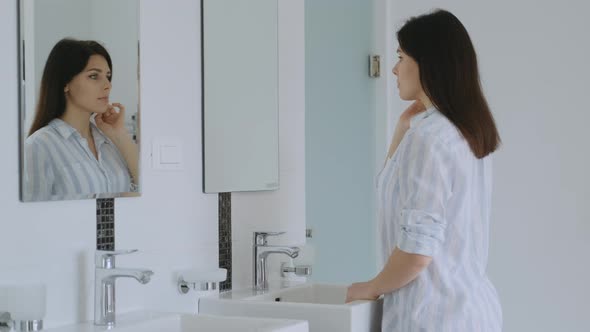 Calm brunette woman in comfortable clothes looking at her reflection at the mirror at home