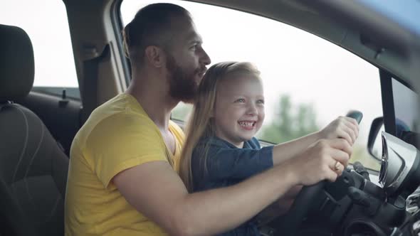 Side View of Happy Father Kissing Head of Laughing Little Daughter Imitating Riding Turning Steering
