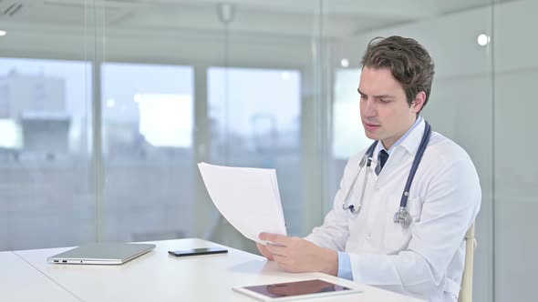 Hardworking Young Doctor Reading Documents in Office