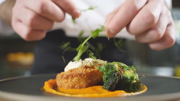 Closeup of a Faceless Chef in a White Uniform Decorating a Platter of Cutlets and Pumpkin Puree in