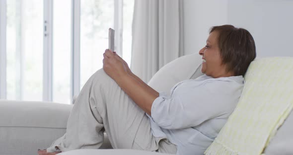 Happy african american senior woman sitting on couch making video call using tablet, smiling