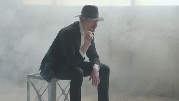Portrait Handsome Confident Man in a Hat Throws Up and Catches the Coin Sitting in an Abandoned