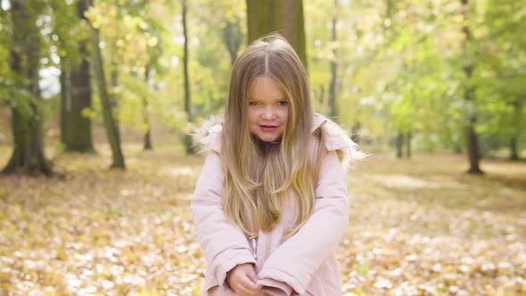 Cute Little Caucasian Girl Talks to the Camera with a Shy Smile in a Park