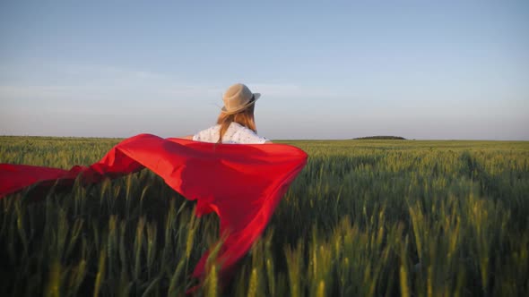 Young Girl Running with Red Tissue in Green Field. Happy Cute Girl Playing in the Wheat Field on a