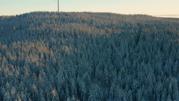 AERIAL - Wind turbine in a snowy forest at sunrise in Sweden, wide shot forward