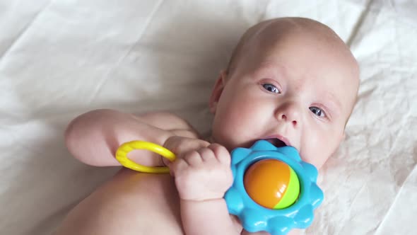 A Newborn Baby Lies on Napkin on Back with a Toy in Hands and Tries To Nibble It