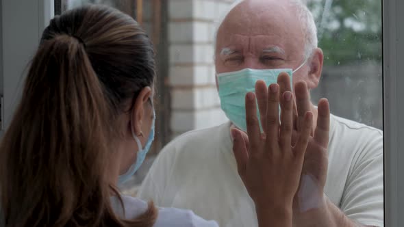 Man And Woman Touch Palms Of Their Hands Through Glass Window In Quarantine