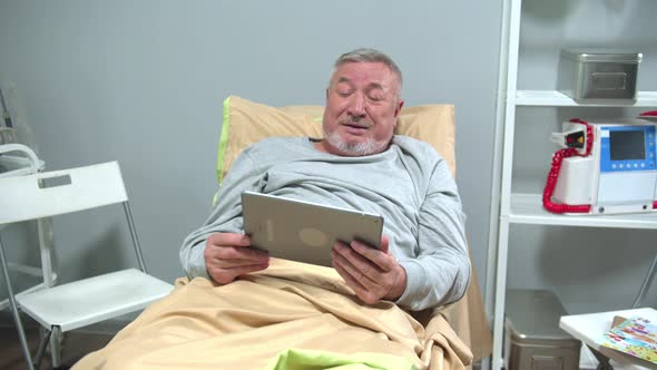 Man Lie on Bed and Talk with Someone on the Tablet and Wave His Hand