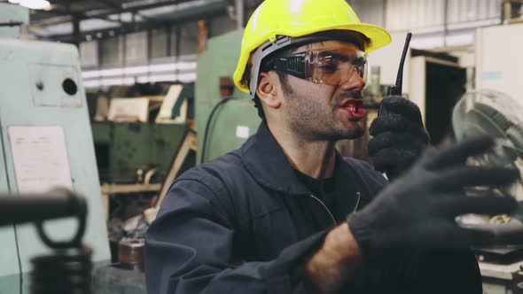 Factory Worker Talking on Portable Radio While Inspecting Machinery Parts