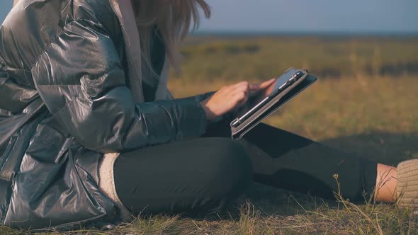 Girl Tourist Works on Tablet Sitting on Grass Closeup