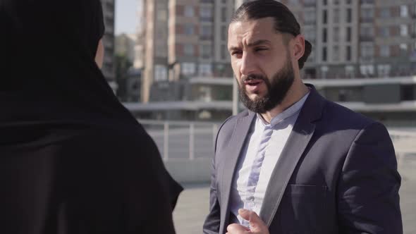 Mad Middle Eastern Man Scolding Unrecognizable Muslim Woman Outdoors. Portrait of Handsome Bearded