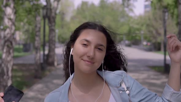 Funny Girl with Long Hair Walks Down the Street and Dances While Listening To Music with Headphones