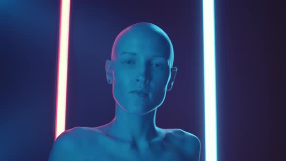 Shirtless Bald Woman Smiling at Camera in Dark Studio with Neon Light
