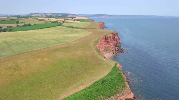 4K Aerial, flying slow over red cliffs by a UK coastal town during summer holiday