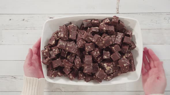 Flat lay. Step by step. Macadamia fudge cut in small cubes on a white serving dish.