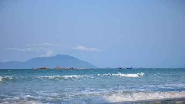 Beautiful Sea Waves with Large Sea Foam Against the Background of the Island and Two Asian Boats