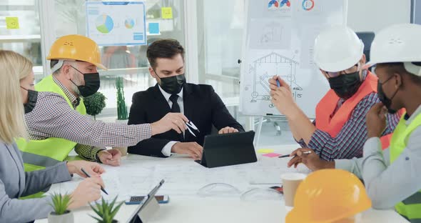 Engineers in Masks Discussing Building Details with Confident Boss During Meeting in boardroom