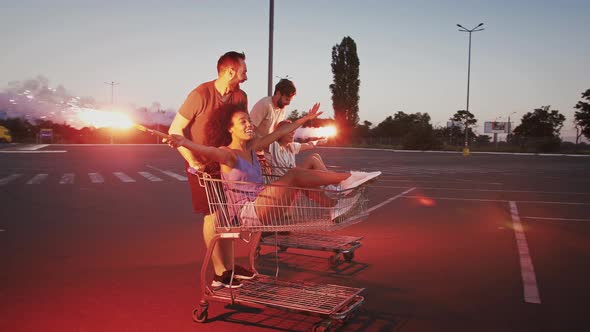 Guys Riding and Spinning on Shopping Trolleys with Their Girlfriends at Deserted Parking Lot