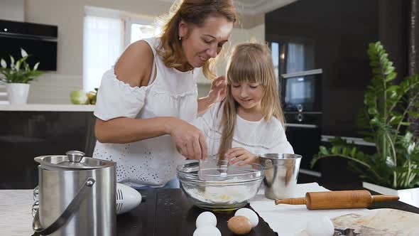 Little Girl Helping her Mom in the Kitchen by Stirring the Ingredients