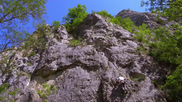 Mid view of man rock climbing in Turda Gorge. Rock walls reach up to blue sky with ropes hanging. Pa