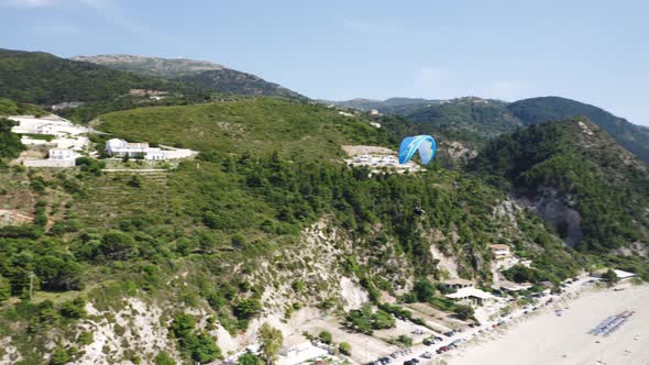 Drone shot of paraglider flying over the sea and hills.