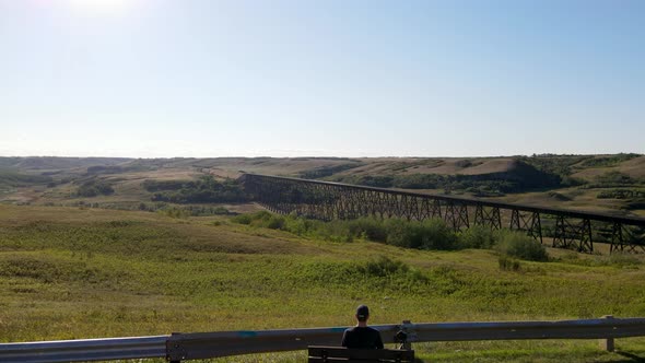 Battle River Trestle on sunny day. Aerial 4K Drone footage of person sitting on a bench enjoying the