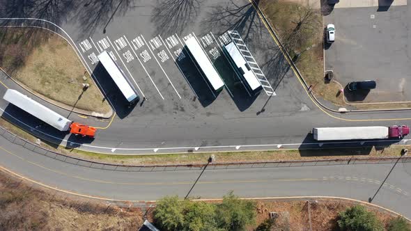 A top down shot over two trucks pulling in to a truck stop on a sunny day. The camera, pointing stra