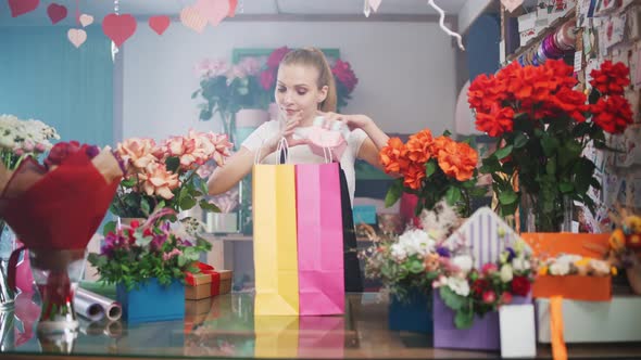 Cheerful Female Florist Packs Boxes with Plants and Gifts in Colored Paper Bags Young Woman Working