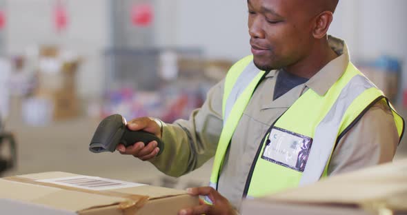 African american male worker wearing safety suit and scanning boxes in warehouse
