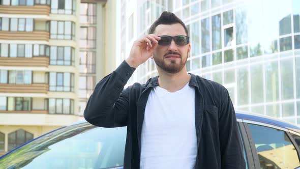 Successful Smiling Confident Young Businessman with Glasses Near Luxury Car in Large Business Center