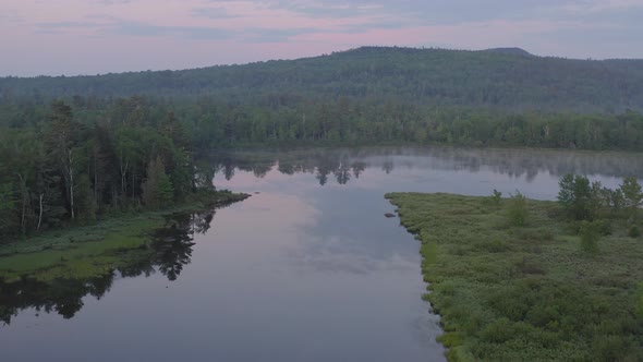 Dawn aerial gliding over flat calm lake covered in thin fog looking over wilderness