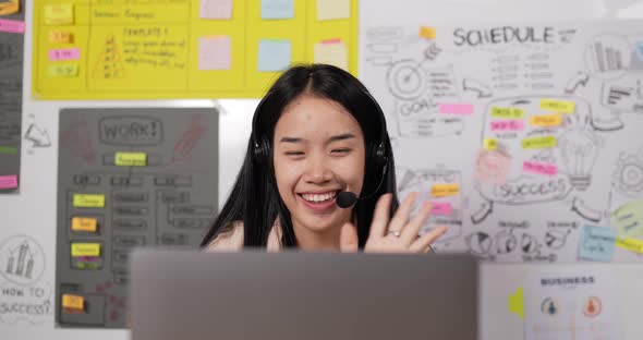 Asian woman with headset using laptop and talking