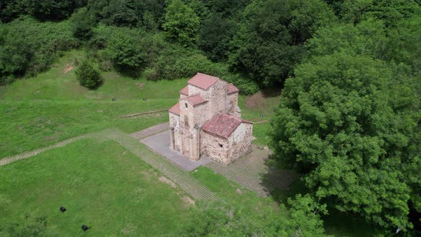 Well-preserved pre-Romanesque church in the middle of a natural green landscape seen from above.