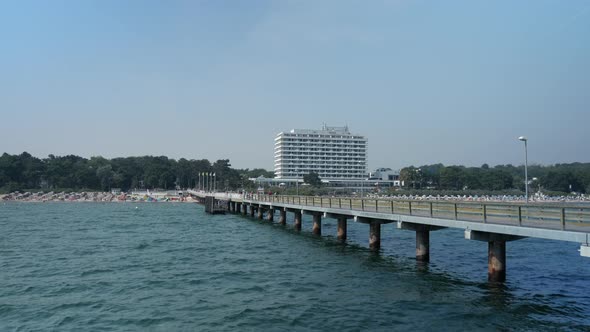Wide shot of long footbridge with sandy beach and famous Maritim Hotel in background in Timmendorf,G