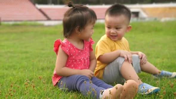 Little Boy And Little Girl Sitting On Grass