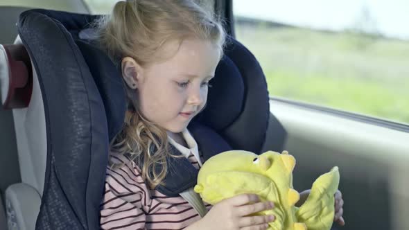 Little Girl Playing with Dragon Toy in Car