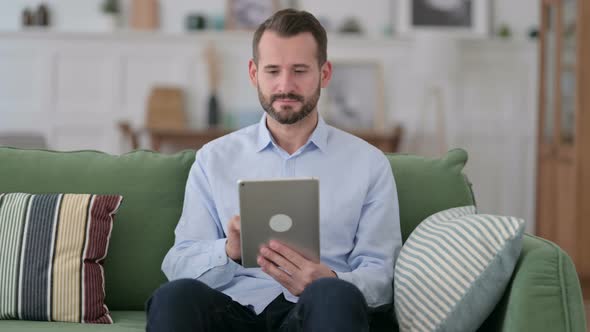 Young Man Using Tablet While Sitting on Sofa 