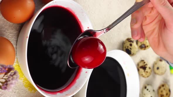 Caucasian Child Paints an Easter Egg with a Metal Spoon and Dips It Into a White Bowl with Red Dye